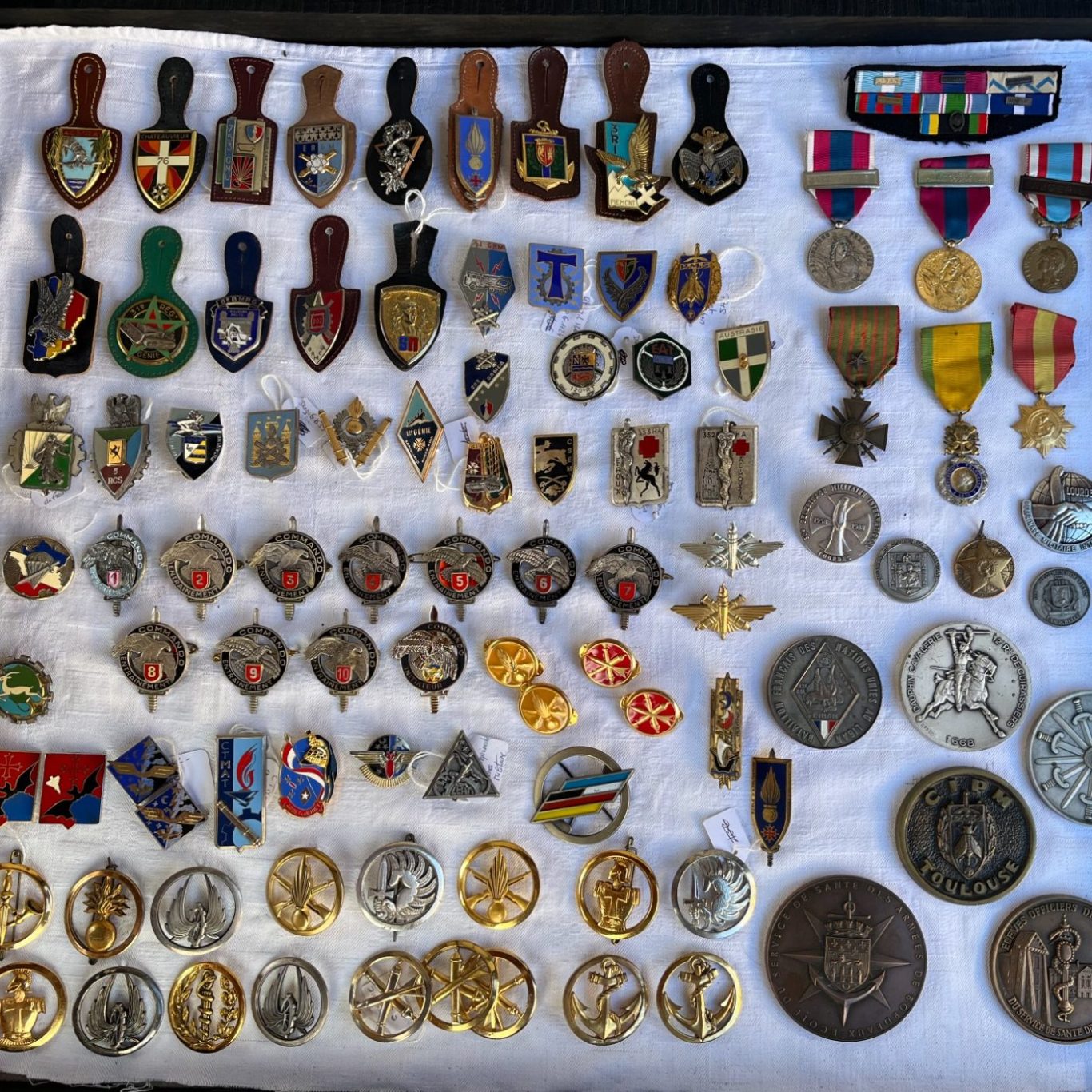 destock-and-compagny, le coin des collectionneurs, insignes armée de terre Collection de médailles militaire, insignes armée de terre variés disposés sur un tissu blanc dans une vitrine